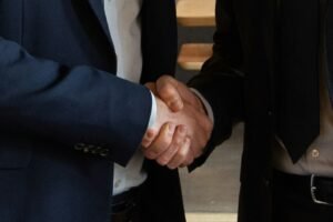 Close-up photo of two business professionals in suits shaking hands, representing a completed domain brokerage negotiation