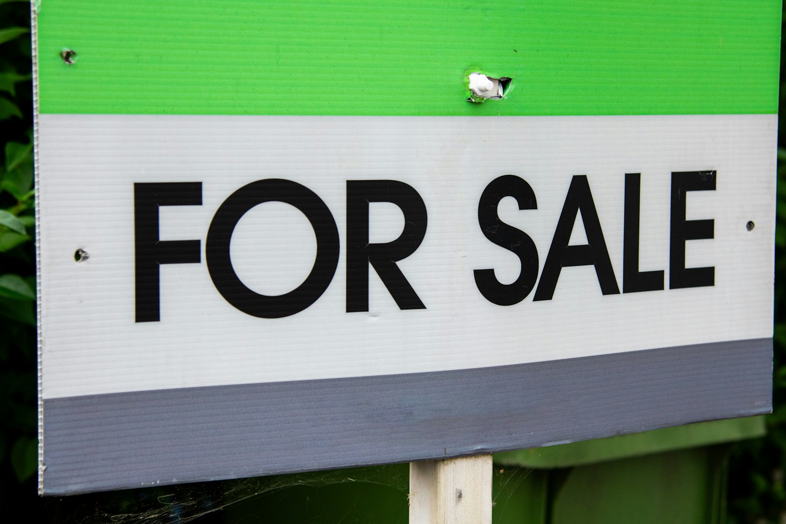 A green and white For Sale real estate sign posted in front of a property